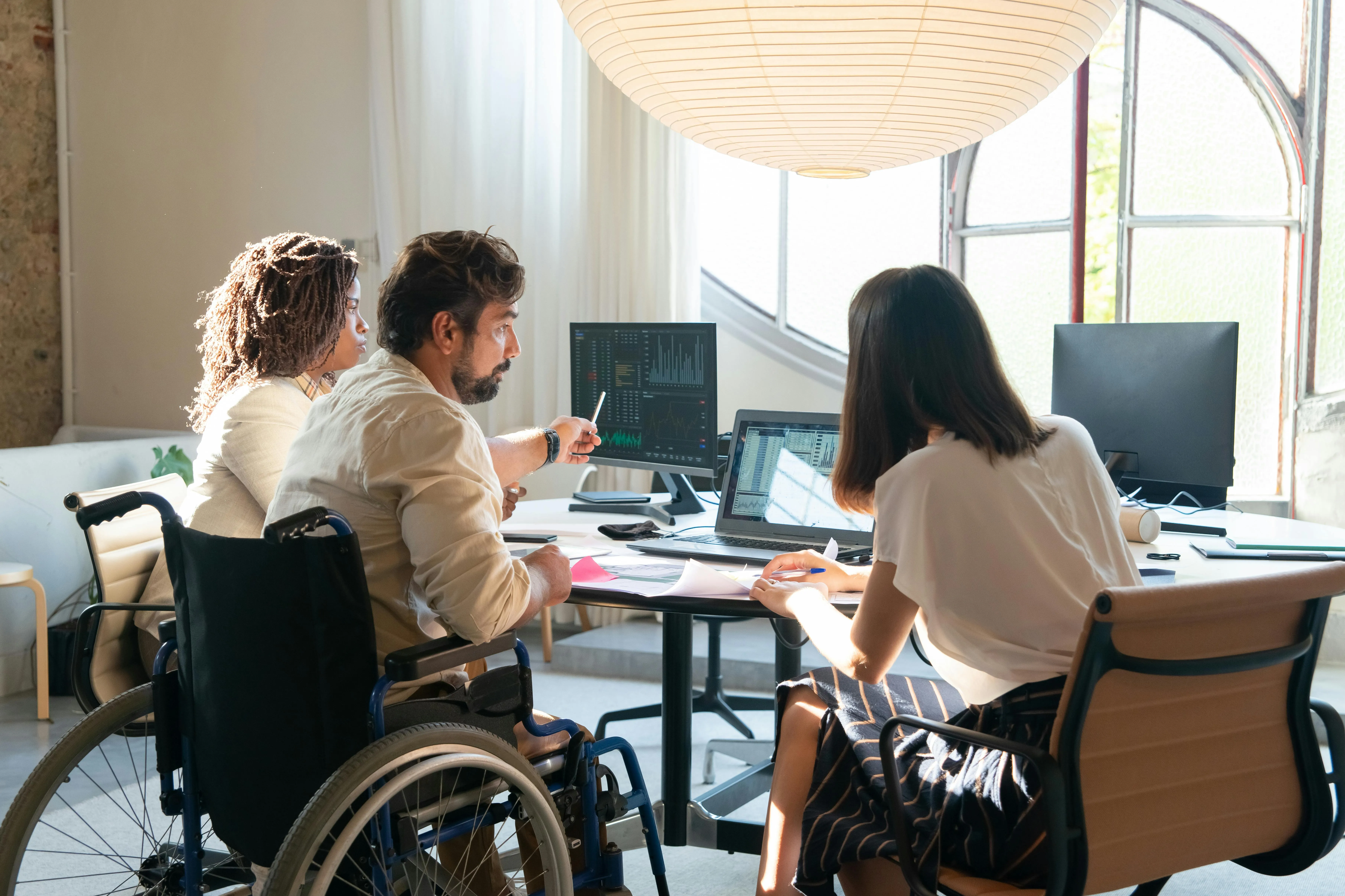 Three people sitting around a desk in an office looking at a computer monitor 