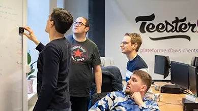 Four men are writing on a whiteboard in front of the Teester company sign.