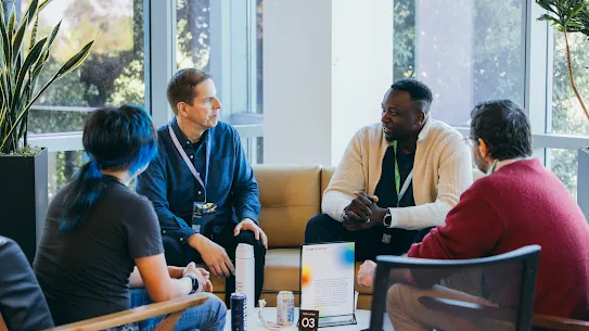 A group of colleagues engaged in a collaborative discussion around a table in a bright office meeting space.