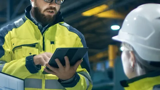Workers in yellow vests and white hard hats using a computer