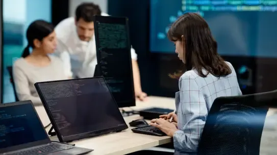  three professionals looking at multiple computer screens with lines of code