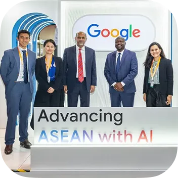 Five diverse professionals in business attire stand smiling in front of a white wall featuring the Google logo and a sign that reads "Advancing ASEAN with AI." A blue arched structure is visible in the background.