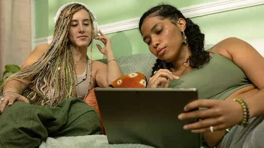 Two women lounging on a couch looking at a tablet screen.
