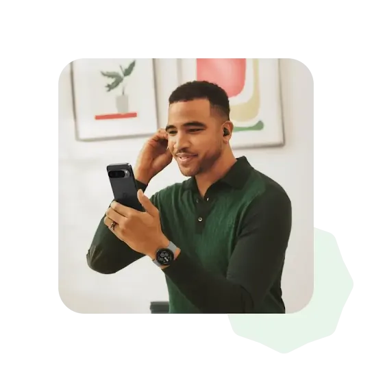 A person wearing a dark green, long sleeved shirt is adjusting one of their earbuds while taking a video call.