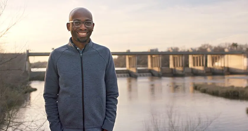 Founder Seyi Fabode smiles at the camera standing in front of a body of water in Texas.