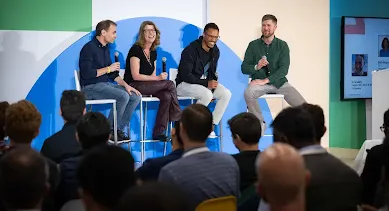 Três homens e uma mulher sentados em cadeiras, segurando microfones no palco.