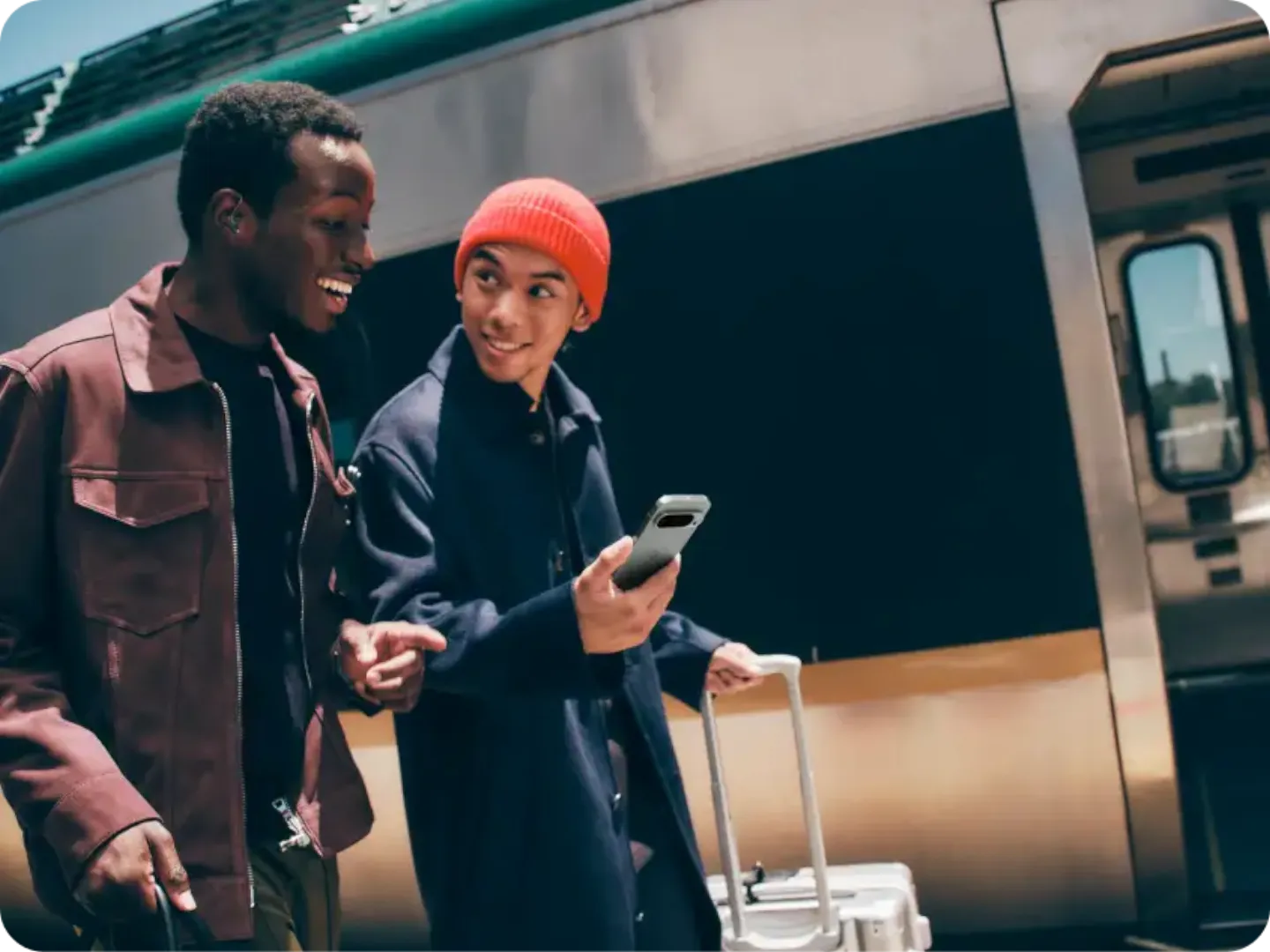 Two men are walking together outside of the train. One of the men is holding a Pixel 9 in his hand.