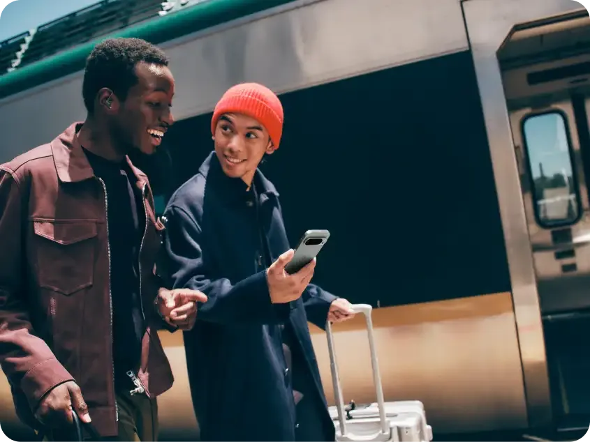 Two men are walking together outside of the train. One of the men is holding a Pixel 9 in his hand.