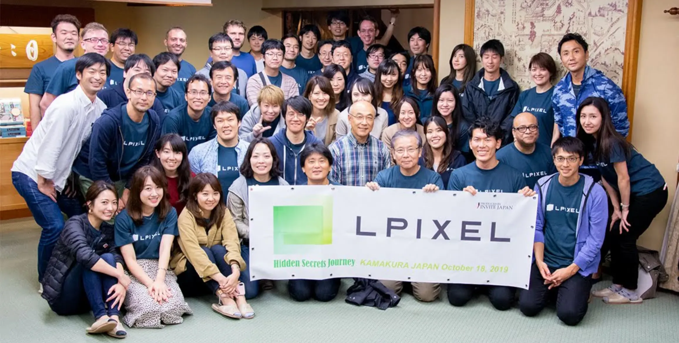 The team of LPixel surrounds a banner revealing their company’s name.