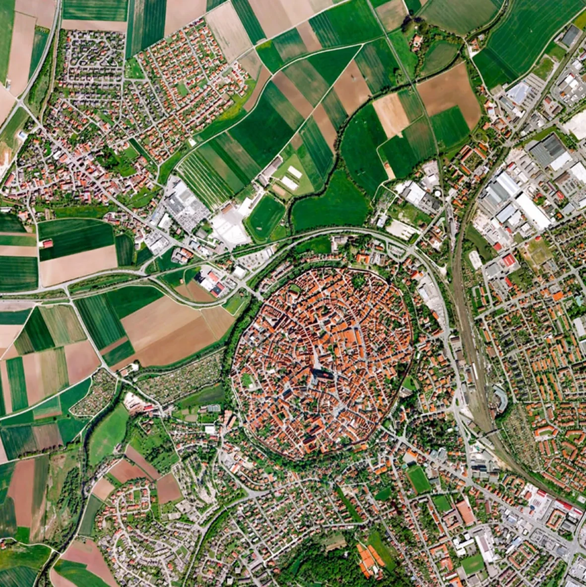 Top-down satellite view of a town featuring a distinct, densely packed circular historic center with red roofs