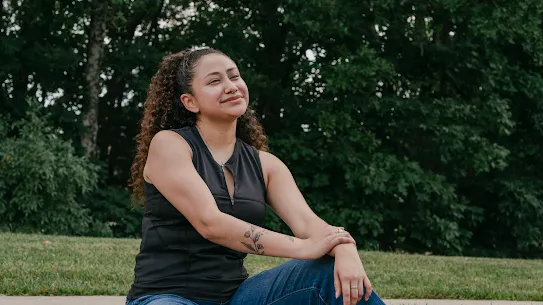 A recent Google Skilled Trades and Readiness Program graduate sits outside on the curb, smiling.