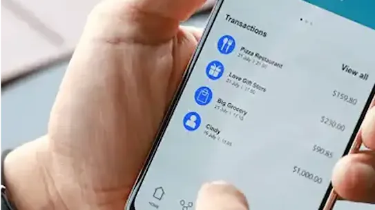 A mobile phone user holds their device in the palm of their hand and reviews recent transactions on their mobile banking app.