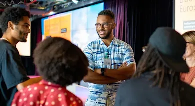 Man wearing a blue shirt talking to a group of people.