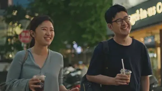 Founders, Suji and Han, are walking with drinks in their hands along a dimly lit sidewalk.