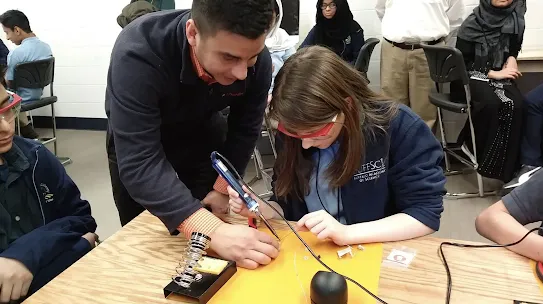 Thimble.io founder Oscar Pedroso assists a student as she practices soldering an electronic component onto a circuit board during a STEM workshop.