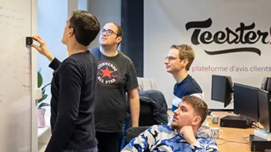 Four men are writing on a whiteboard in front of the Teester company sign.