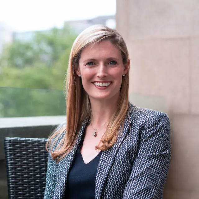 Professional headshot of Alexandra Reeve Givens, CEO of the Center for Democracy & Technology, smiling and wearing a patterned blue blazer while seated outdoors.