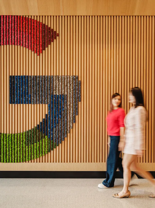 Two people walking past a wall with a large Google G logo on it.