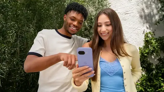 Duas pessoas ao ar livre, sorrindo e olhando para um smartphone Pixel roxo. O homem aponta para a tela do smartphone que a mulher está segurando.