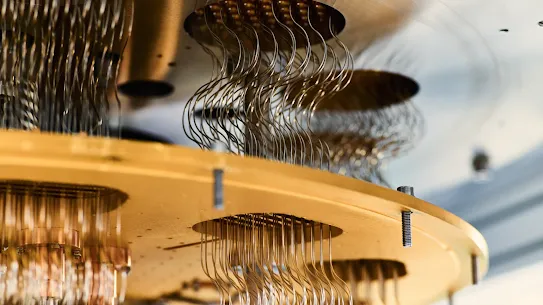 An extreme close-up view of the intricate internal hardware of a quantum computer. The image shows gold-plated plates and hardware components connected by bundles of extremely fine, wavy, silver-colored coaxial cables running vertically between the circular cutouts of the metallic tiers.