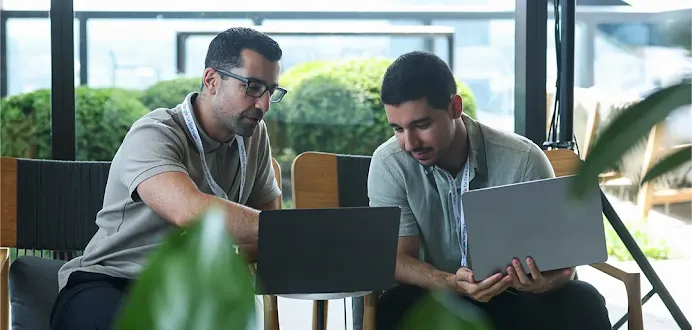 A man working on a laptop while talking to a colleague.