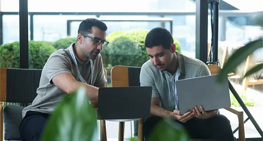 A man working on a laptop while talking to a colleague.