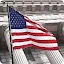 A close-up shot of the American flag waving in front of a classical stone building with large columns.