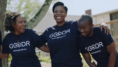 Group of coworkers wearing matching shirts smiling and holding shoulders