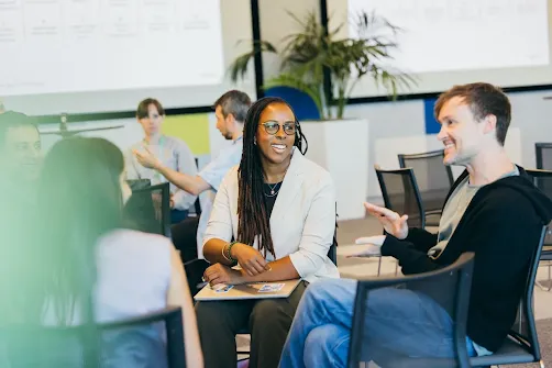 A smiling woman listening to a male colleague during a casual office meeting.