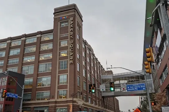 Exterior view of the historic Bakery Square brick building featuring vertical signage, a Google logo near the top, and a skybridge connecting across the street