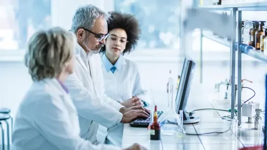 three scientists reviewing information on a laptop in a lab