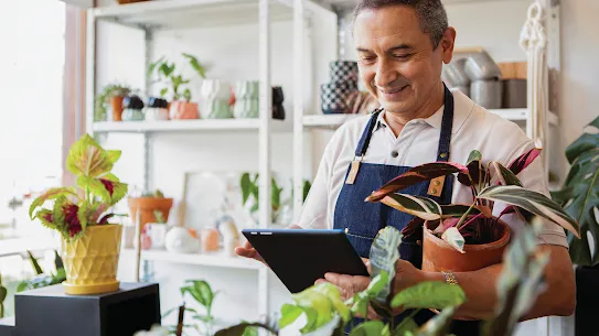Man holding a tablet, standing in a flower store surrounded by vibrant flowers and plants.