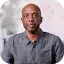 Portrait of James Manyika, Google’s Senior Vice President of Research, Technology, and Society. He is a Black man with a shaved head, wearing a grey button-down shirt, looking directly at the camera with a neutral expression. The background is a soft-focus office setting. This image accompanies his commentary on AI disruption and its societal impact for the Google and Forbes partnership.
