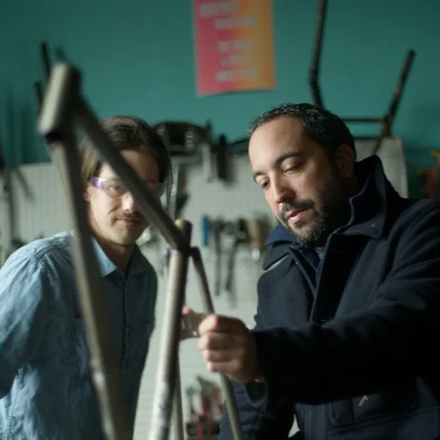 Two people work on a mechanical part in a garage setting.