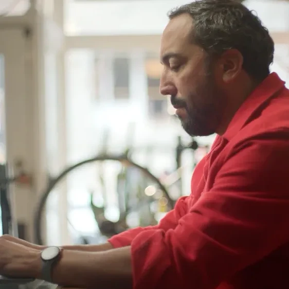 A person sit at a laptop in their kitchen, concentrating hard on what's on the screen.