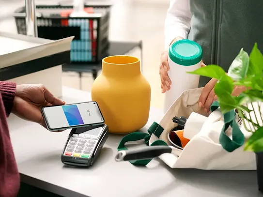 A person using a smartphone to make a Tap and Pay contactless payment at the checkout counter.