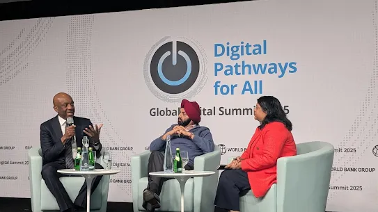 A panel discussion at the Global Digital Summit 2025 titled "Digital Pathways for All." Three speakers are seated in light blue armchairs on a stage: a man in a suit speaking into a microphone, a man in a blue sweater and red turban listening, and a woman in a red blazer looking toward the speaker.