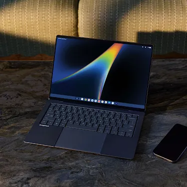 Googlebook open on a marble table with a phone nearby.
