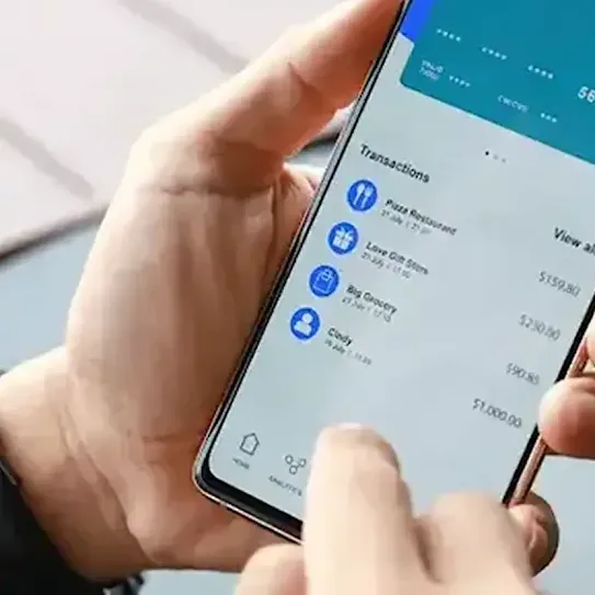 A mobile phone user holds their device in the palm of their hand and reviews recent transactions on their mobile banking app.