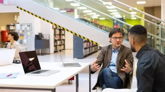 people with laptops working together at a table in the library