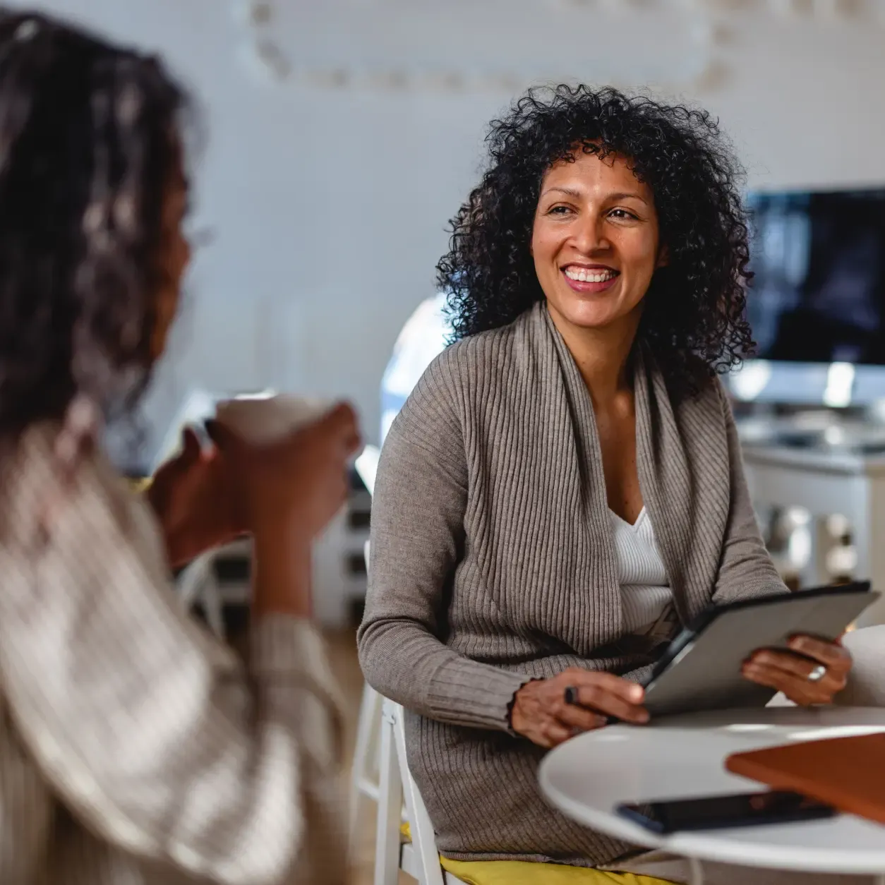 Two colleagues collaborate in a public setting, one holding a tablet and actively discussing its content with the other