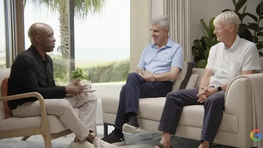 Dr. Mohamed El-Erian (center) and Nobel Laureate Michael Spence (right) engaged in a living-room style conversation with a moderator (left). They are seated on modern beige furniture in a bright room with a large window overlooking a coastal landscape with palm trees.
