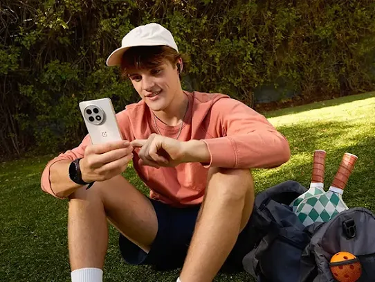 A young man using an Android phone on a grassy field.