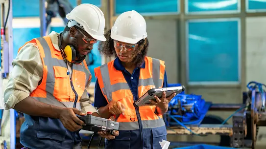 A man and a woman in hard hats looking at information on a tablet.