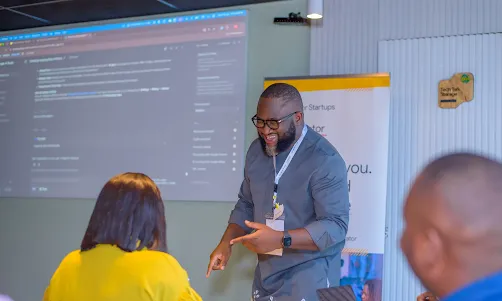 A presenter smiling and speaking at a tech startup workshop.