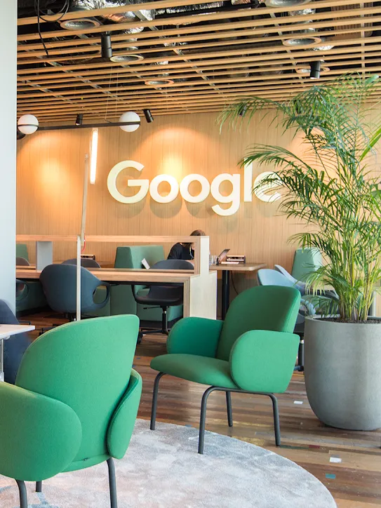 两个人坐在工作区的沙发上，背景是 Google 徽标。