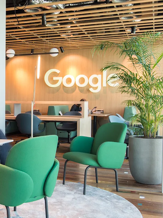 Duas pessoas sentam em um espaço de trabalho com o logotipo do Google ao fundo.