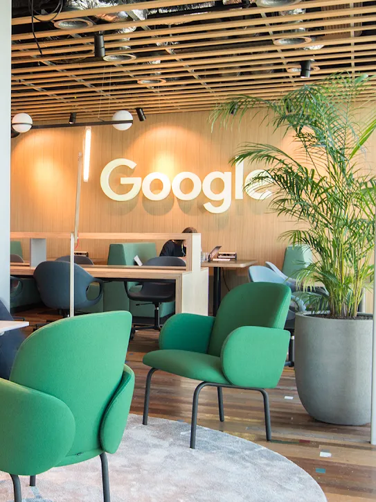 Dos personas sentadas en un espacio de trabajo con el logotipo de Google en el fondo.