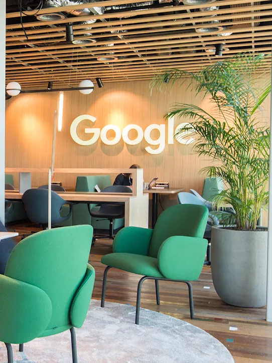 Due persone sedute in uno spazio di lavoro con il logo di Google sullo sfondo.