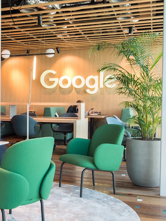 Duas pessoas sentam em um espaço de trabalho com o logotipo do Google ao fundo.